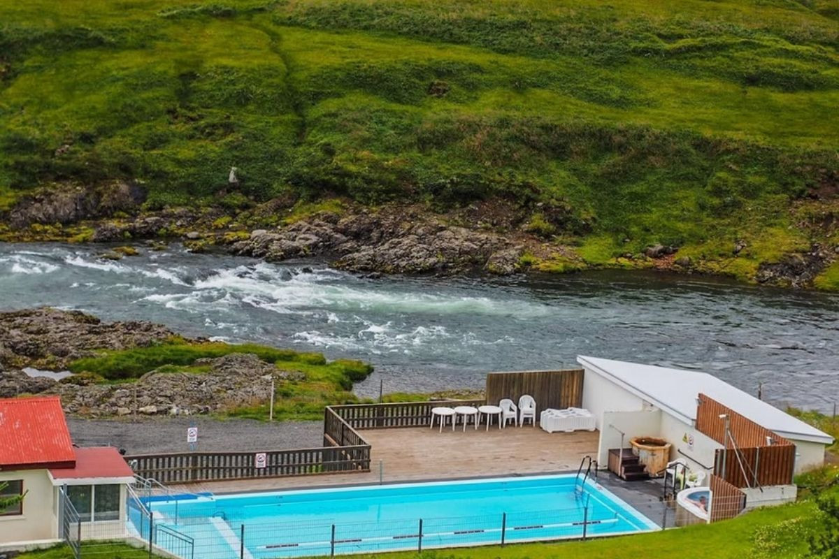 Selárdalslaug, a geothermal pool in Iceland, offers a unique bathing experience next to a river, with a small building and recreational area visible.